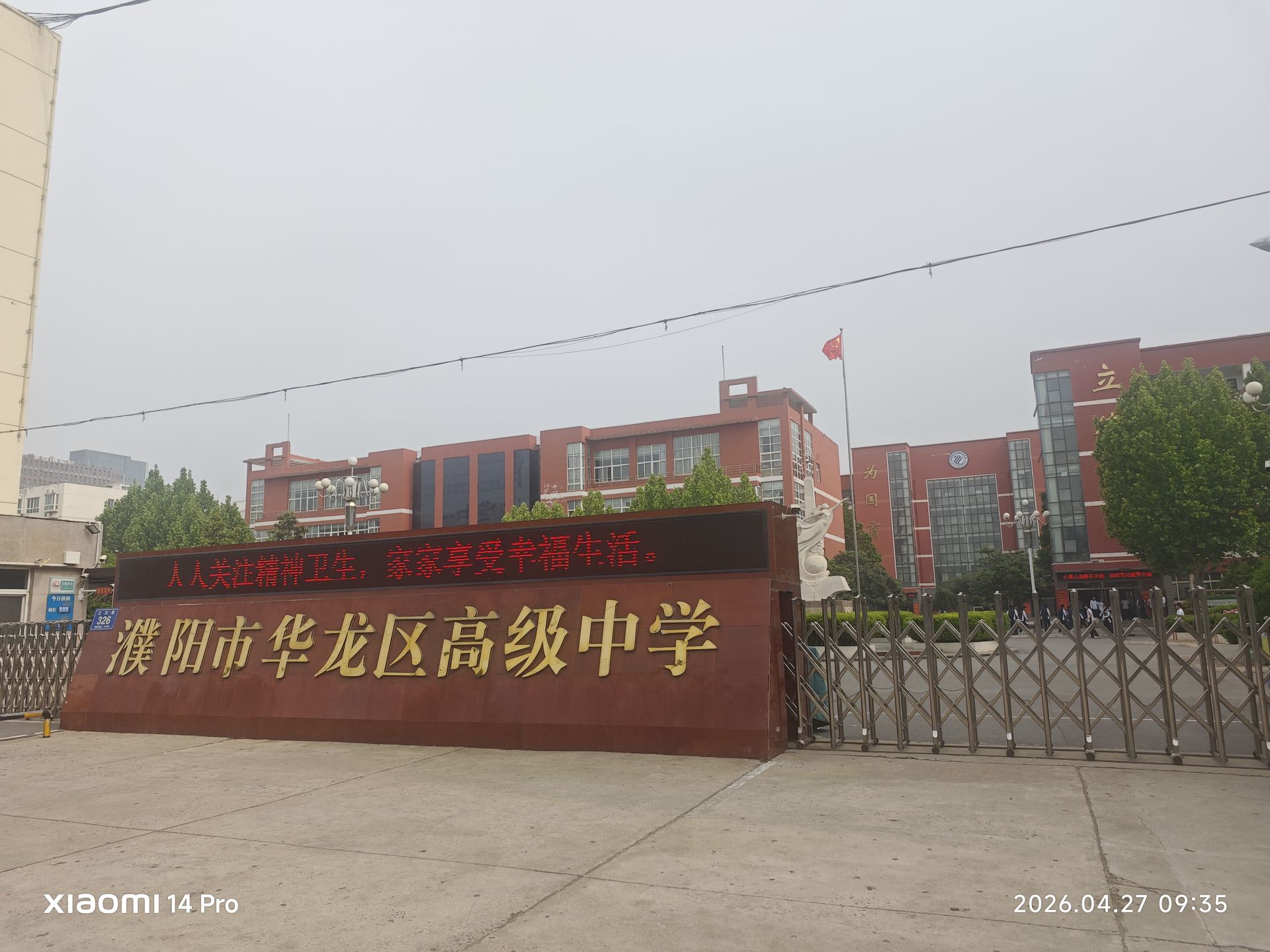 '濮阳市华龙区高级中学'的金字牌匾在晨光中熠熠生辉，铁栅栏门后是莘莘学子的求知路。