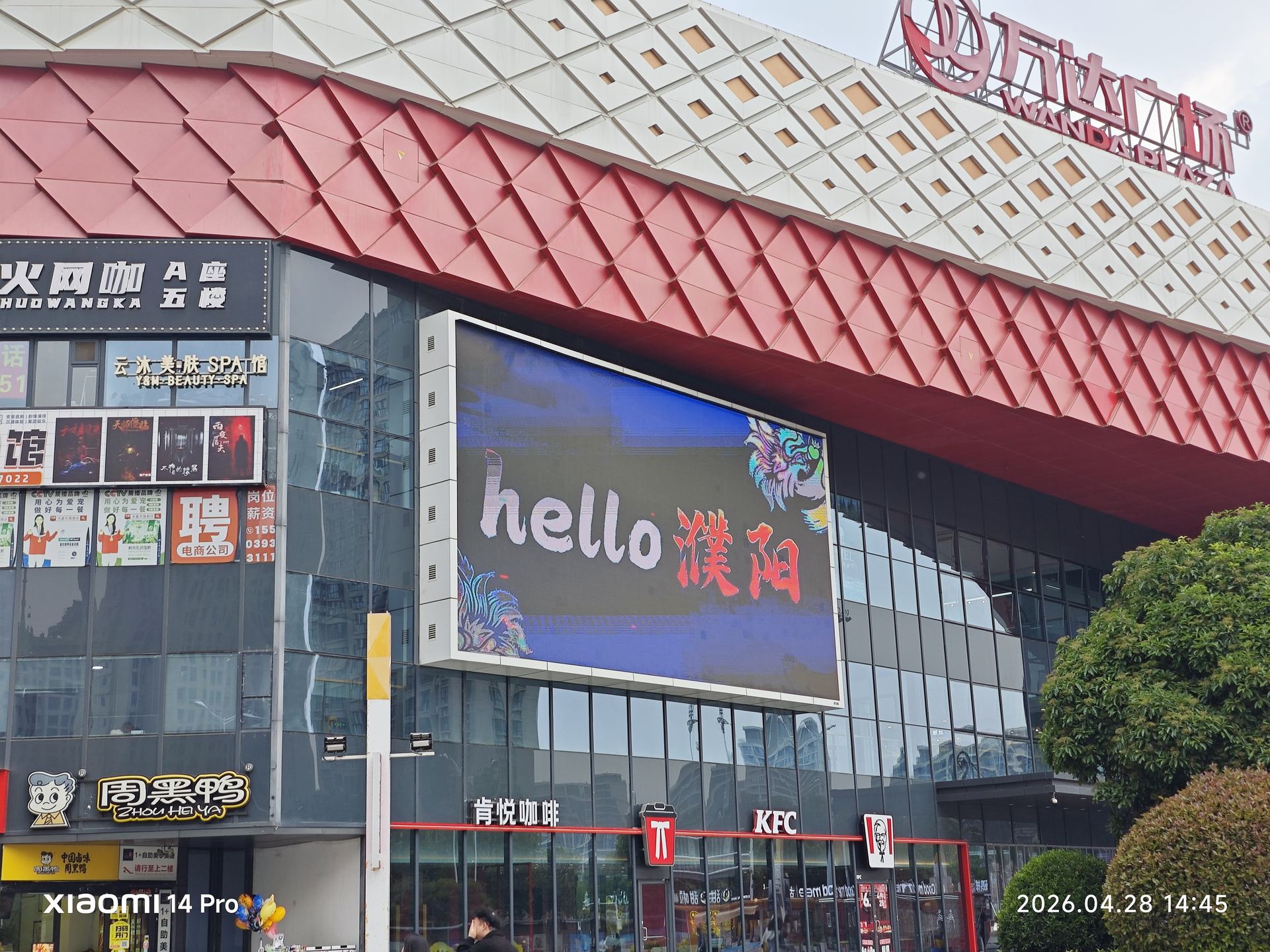 'hello 濮阳'的巨大LED屏闪烁在商场外墙上，红色屋顶下的商业气息活力四射。